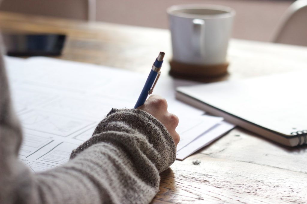 Hand mit Stift über einem leeren Notizblock neben einer Kaffeetasse – Symbolbild für Aufschieben bei ADHS
