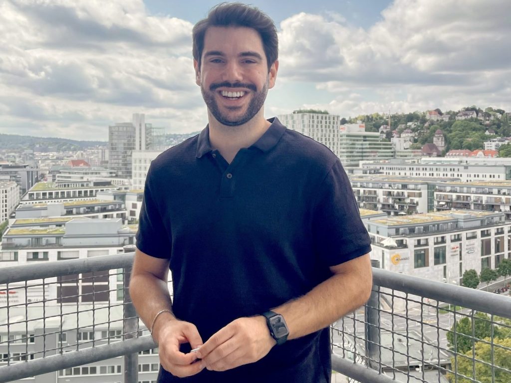 Sezer Yaşar, ADHS-Coach, lächelnd auf einem Balkon mit Blick über die Stadt